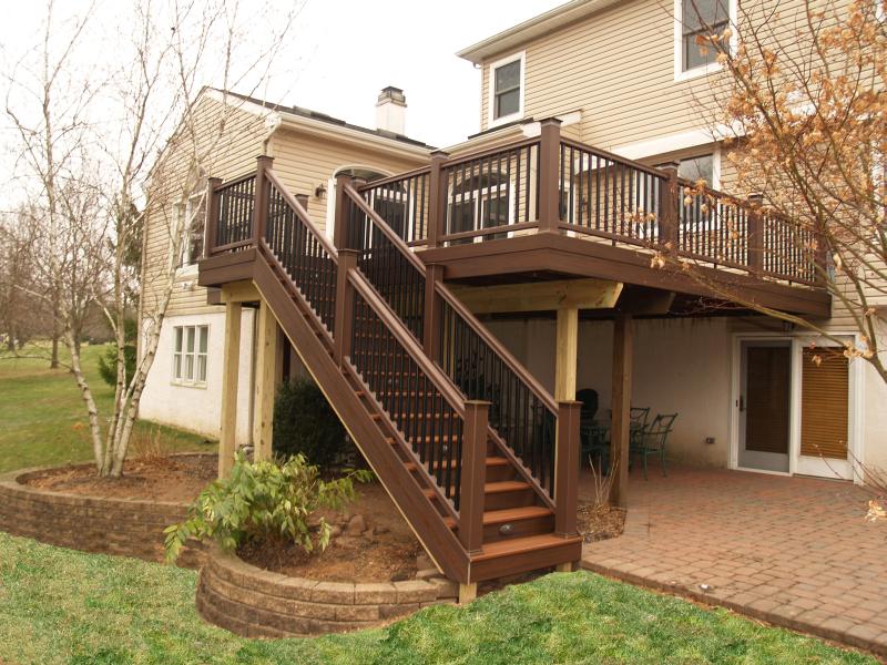 Deck from McHenry Deck Builders with stairs leading up to deck that hangs over a patio.